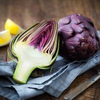 Fresh purple artichokes on dark rustic wooden background with slices of lemon