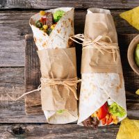 two tortilla wrap and corn chips with avocado dip placed on the wooden platter