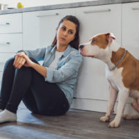 sad woman and dog sitting in kitchen on floor