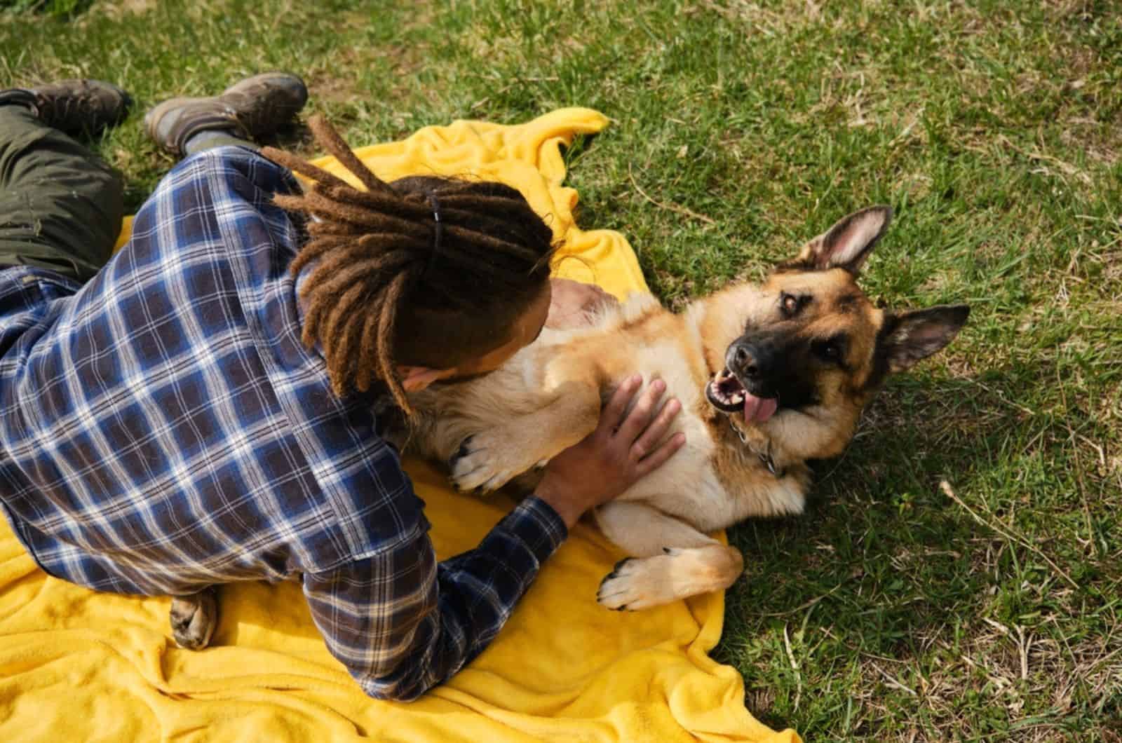 owner and his german shepherd dog lying on yellow blanket