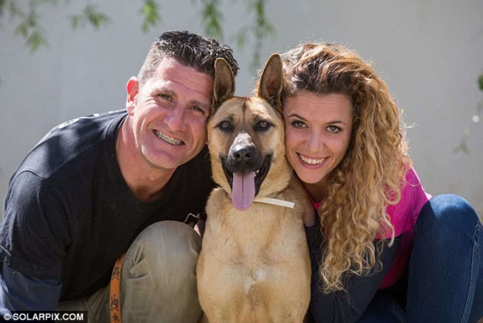 man and woman embracing their dog in the yard