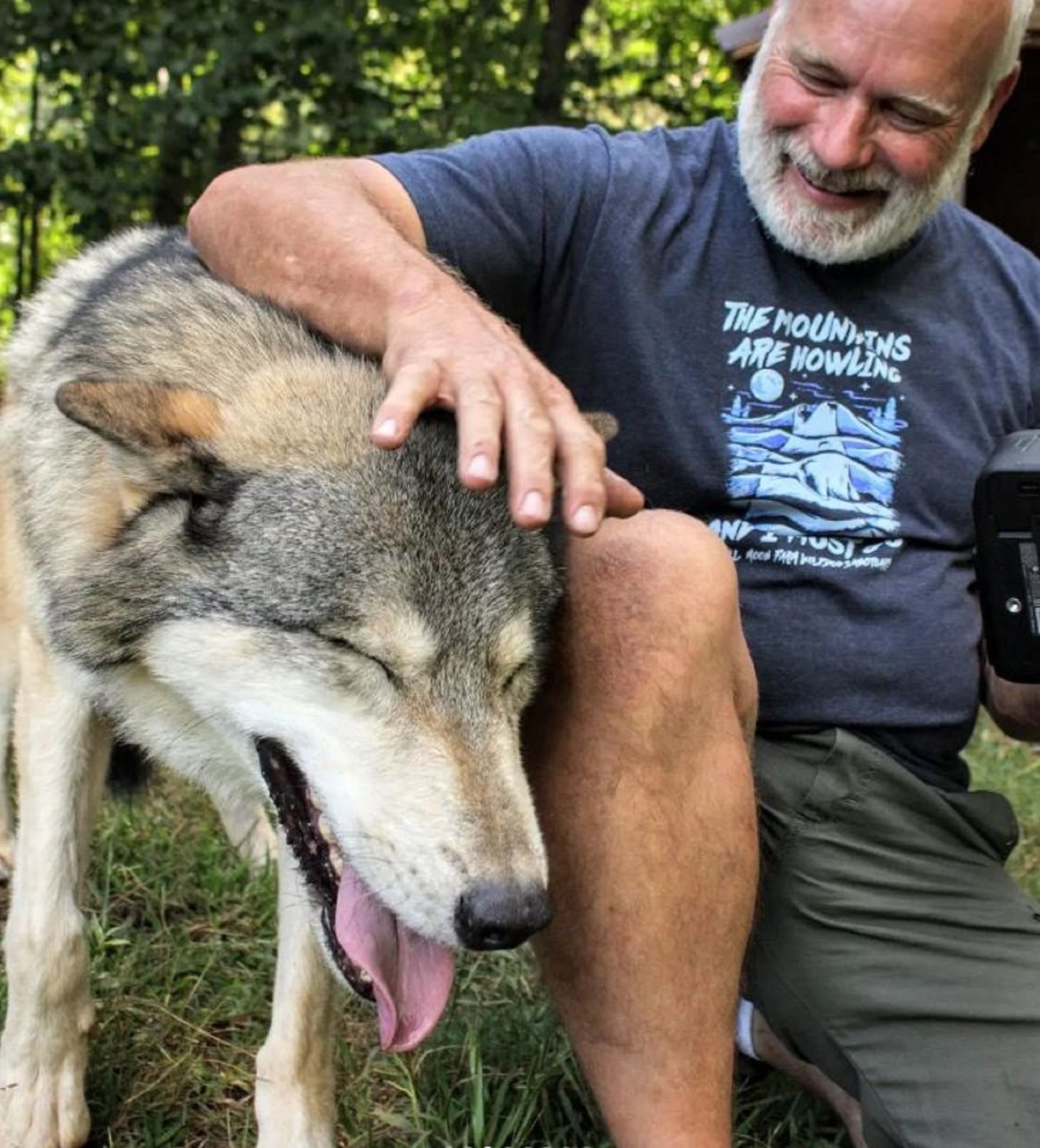 smiling man cuddling his wolf dog in the yard