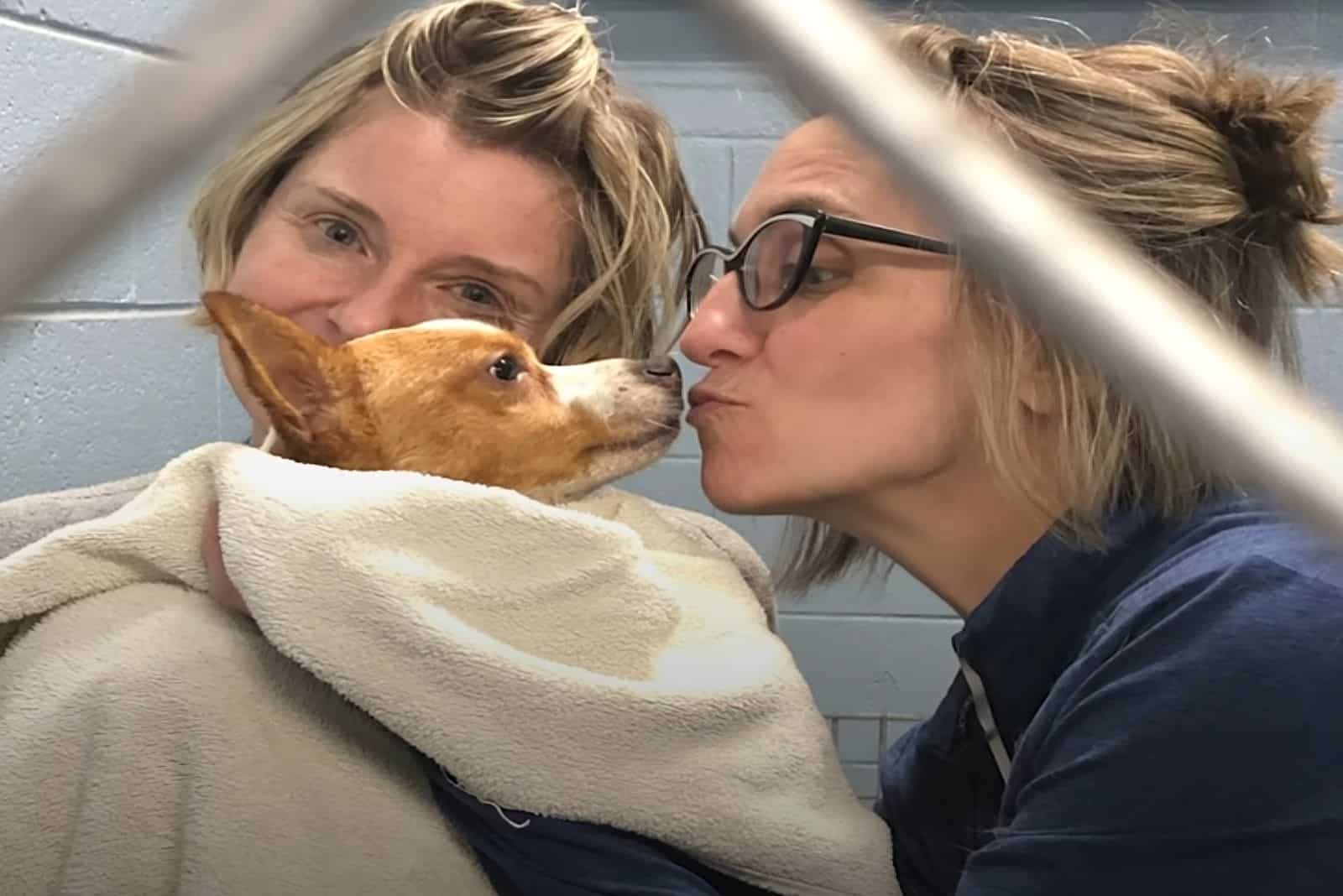 two women hugging and kissing dog they rescued