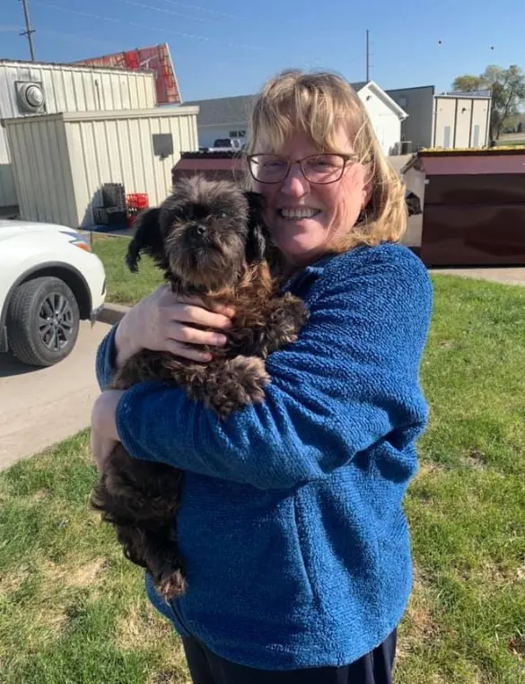 a woman with glasses holds a shaggy dog in her arms