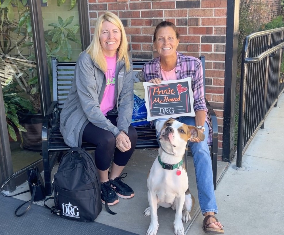 two women are sitting on a bench and a dog next to them