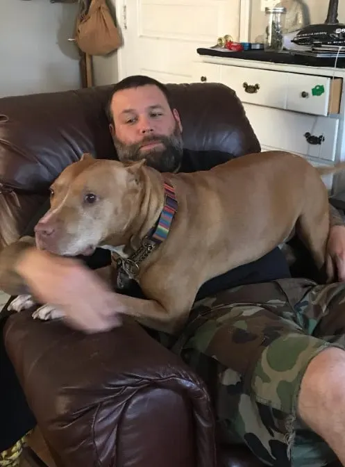 a dog sits on the lap of a man sitting on an armchair