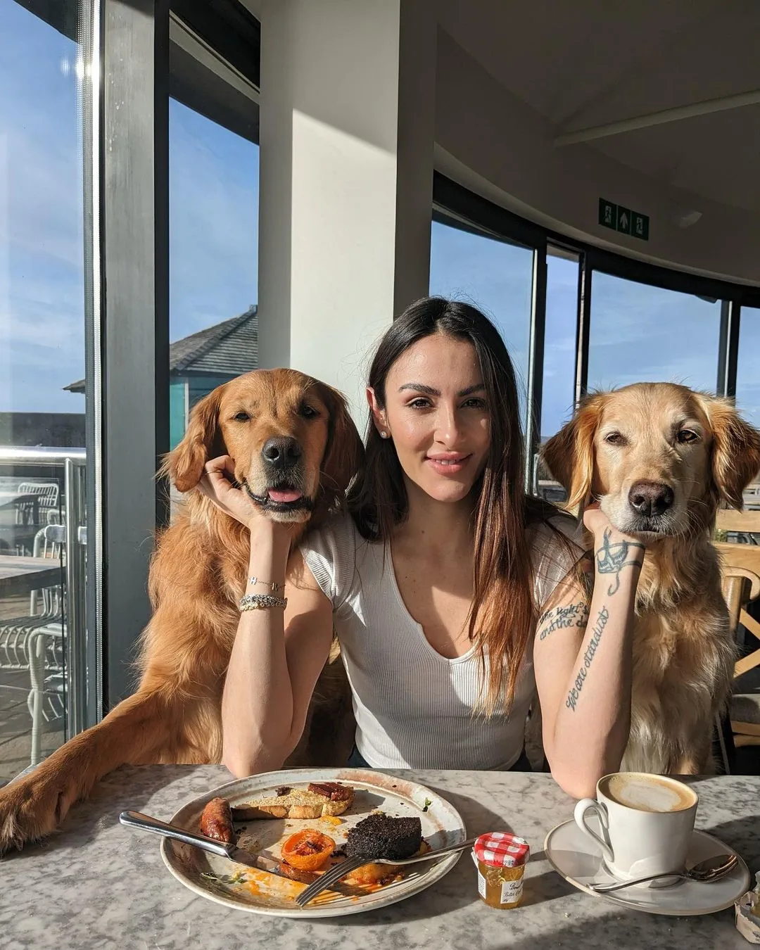 two golden retrievers and woman sitting at table