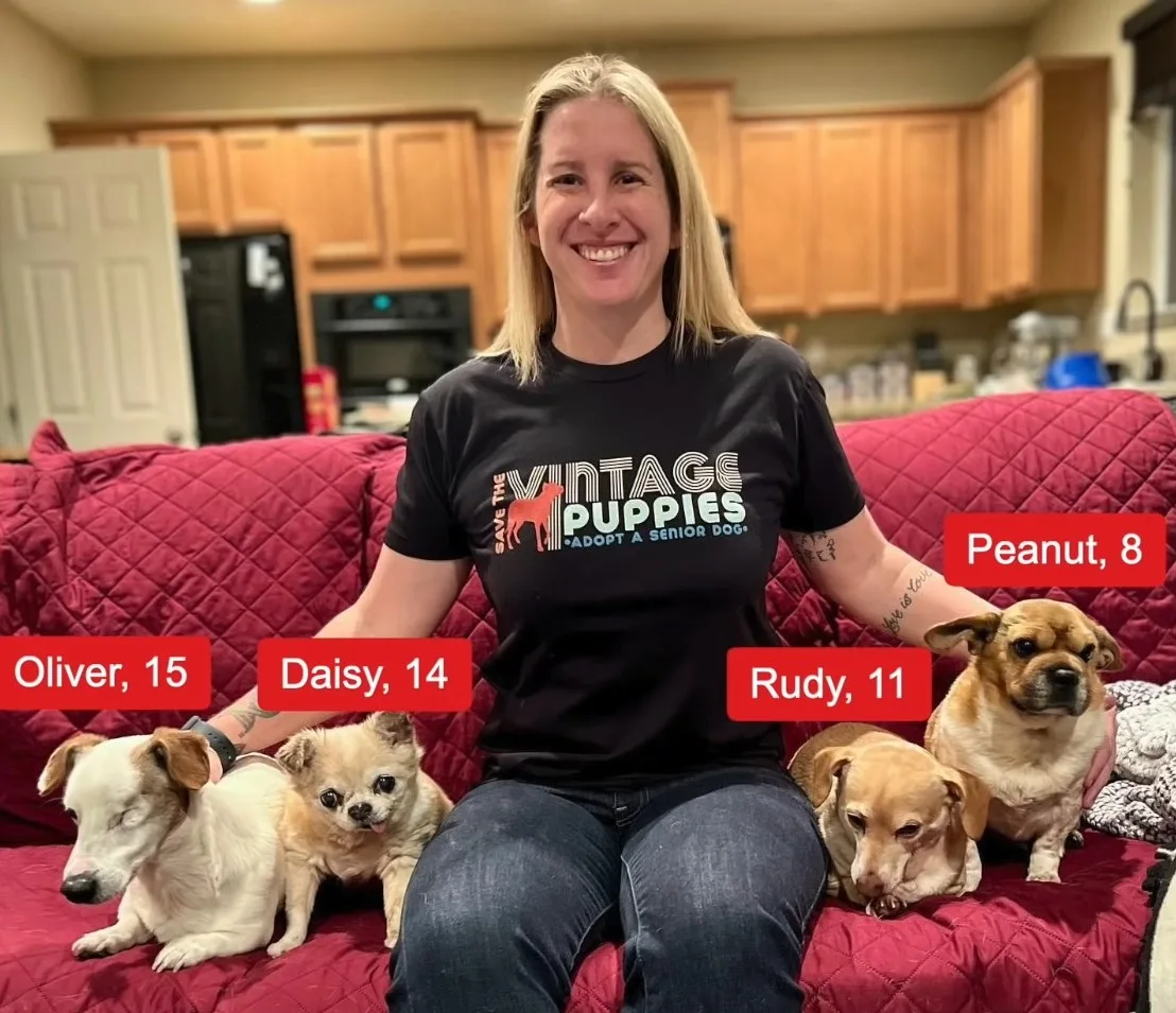 a smiling girl sits on the couch next to her adopted dogs