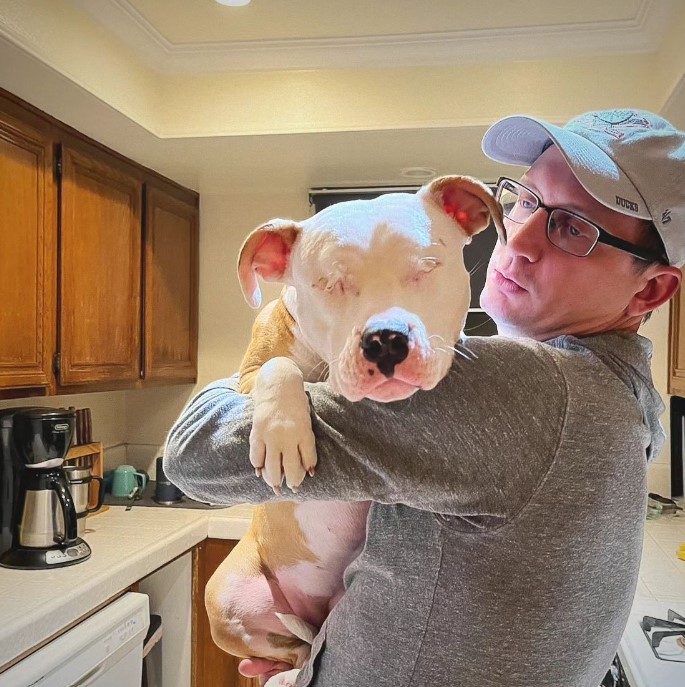 a man holds a blind dog in his arms