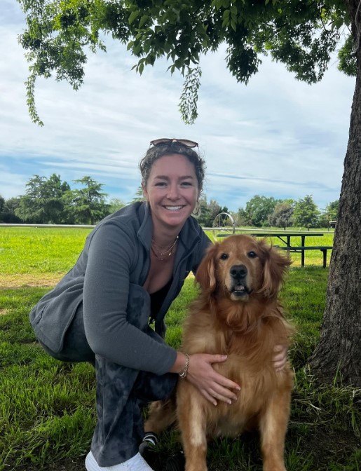 a smiling girl takes a picture with a golden retriever in the park