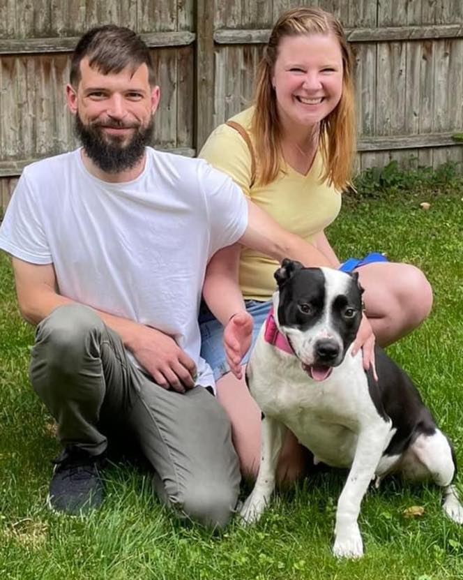 a man and a woman with a playful dog take a picture