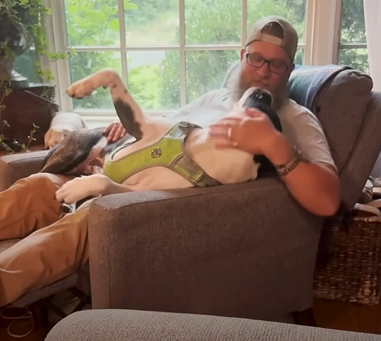 a man sits in an armchair and plays with a dog