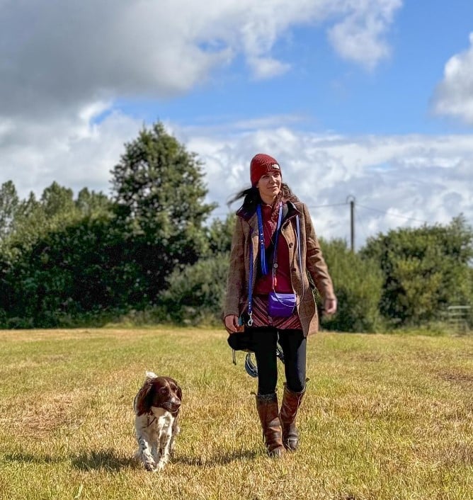 a woman walks with a dog in a field