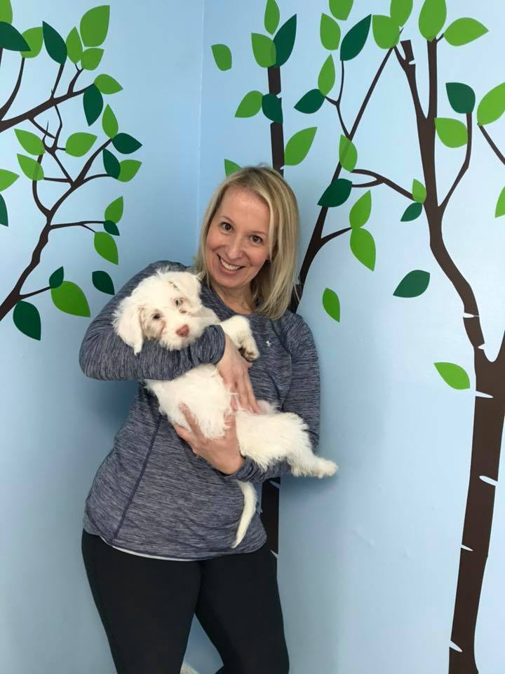 a smiling woman holds a white dog in her hands