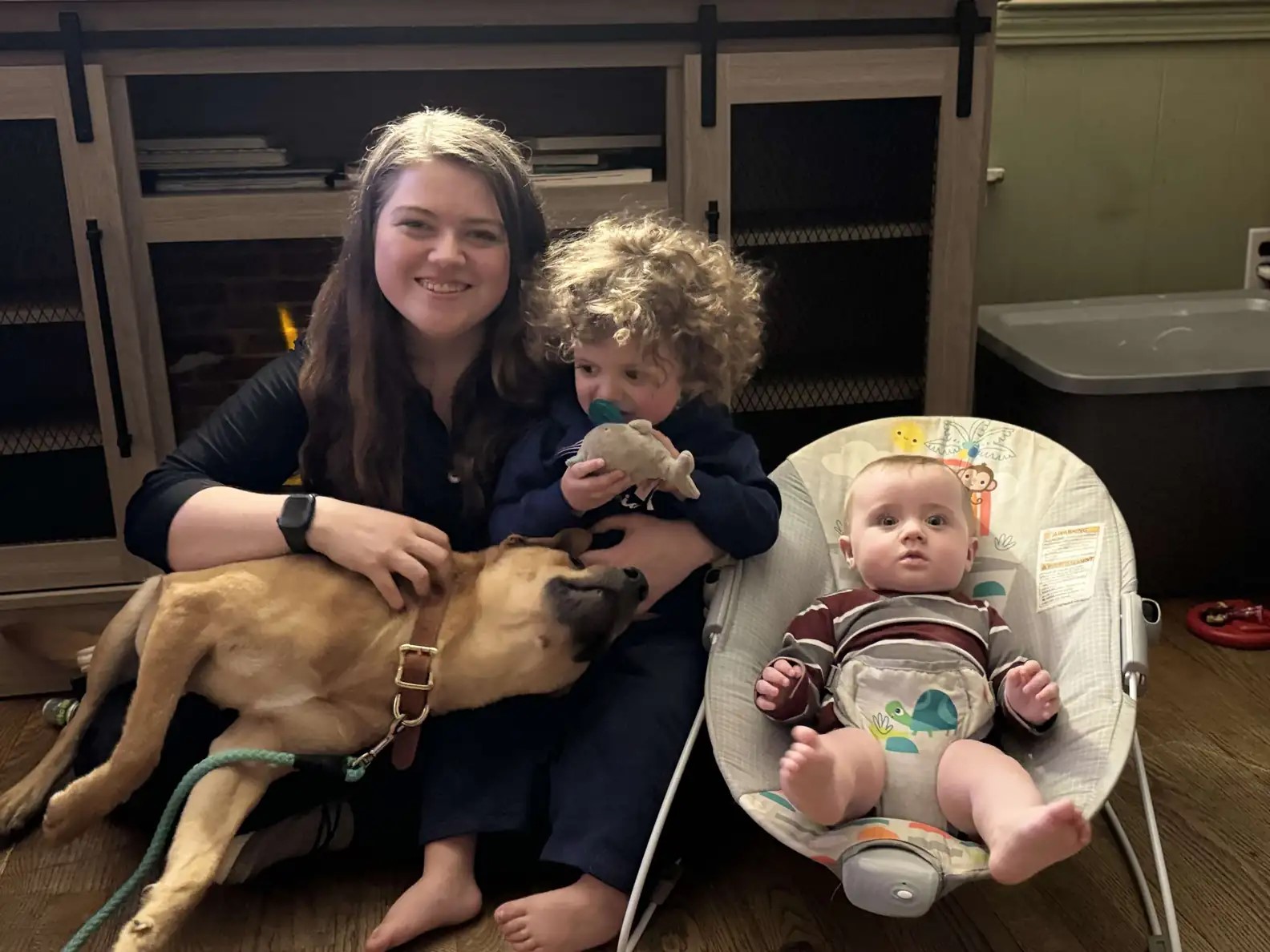 a woman is holding a child, a dog is cuddling