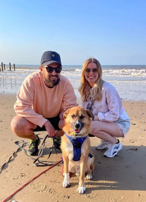 smiling man and woman on the beach with a dog