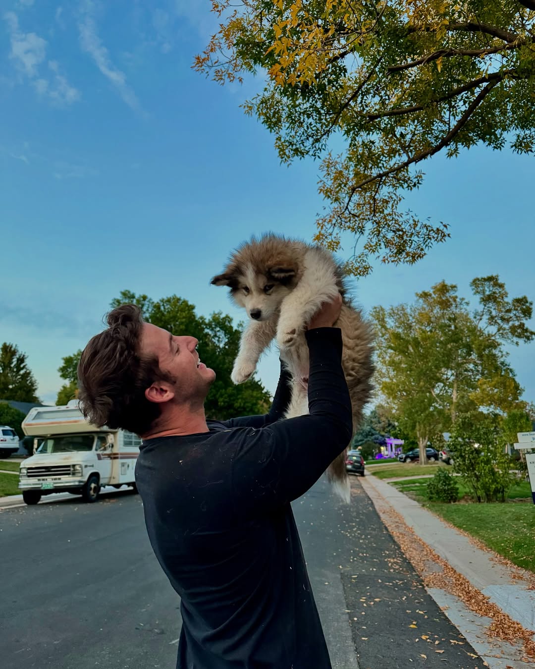 smiling man holding puppy in the air