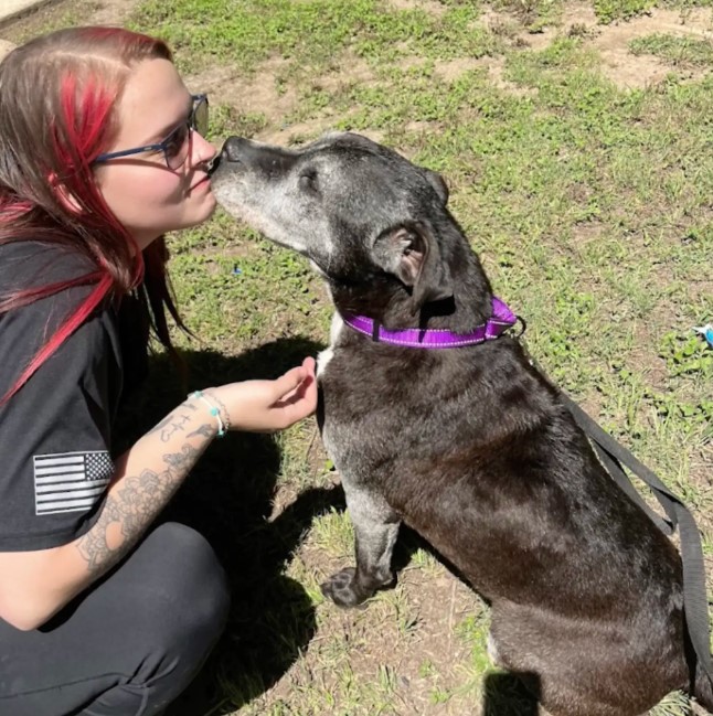 woman kissing a black dog